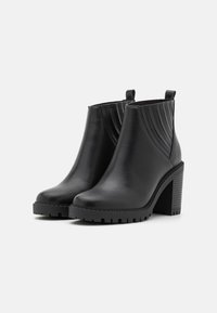 Bottines en cuir noir avec une finition lisse, un grand talon bloc, et un détail à relief à l'arrière. Équipées de languettes pour un enfilage facile.