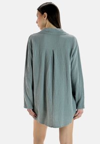 Lichtblauw, oversized lang shirt met lange mouwen, gemaakt van gestructureerde stof, met een kraag en een plooi aan de achterkant. De zoom is licht gebogen.