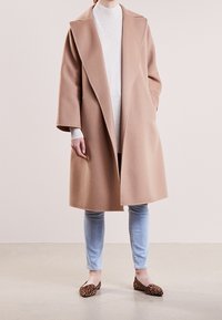 Manteau en laine beige avec de larges revers, manches longues et devant ouvert. Associé à un pull léger, un jean clair et des ballerines à imprimé animal.