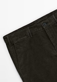 Pantalon en velours côtelé marron foncé montrant la ceinture, les passants de ceinture, la poche avant et la fermeture par bouton sur fond blanc.