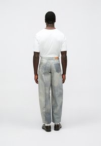 Lysegrå denimbukser med avslappet passform, som har et subtilt falmet mønster, fem lommer og en brun lærpatch på bakre midje.