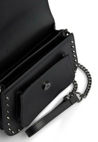Czarna skórzana torba na ramię z srebrnymi ćwiekami na brzegach, prezentująca gładkie wnętrze, przednią kieszeń i łańcuszkowy pasek.