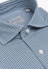 Camisa ajustada en un patrón de espiga azul y blanco. Presenta un cuello, una fila de botones y una etiqueta con "DAN JOHN."