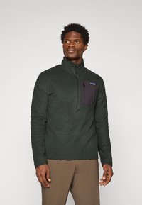 Pull-over en polaire vert avec col haut, zip quart, corps texturé et poche poitrine noire. Présente le logo Patagonia.