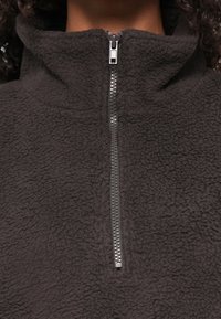 Donkergrijze fleece pullover met hoge kraag en zilveren ritssluiting. Heeft een gestructureerd, zacht oppervlak en een ontspannen pasvormontwerp.