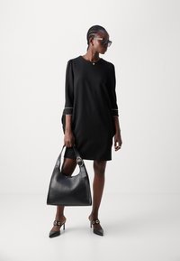 Black short-sleeve dress with white trim, paired with a large black leather handbag and pointed-toe heels featuring circular accents.