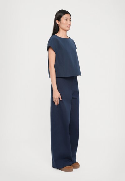 Top court bleu marine à manches courtes associé à un pantalon large de la même couleur, avec une texture lisse et un design minimaliste.