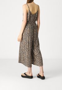 Luipaardprint jumpsuit met V-hals, verstelbare schouderbanden en elastische tailleband. Flare-silhouet, lichtgewicht stof, gecombineerd met zwarte platform sandalen.