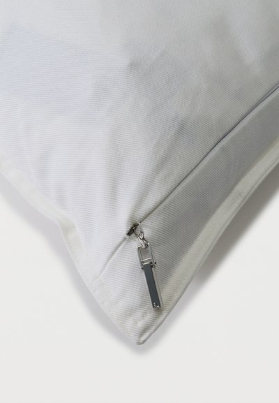Γωνία μαξιλαριού από λευκό υφασμάτινο ύφασμα με υφή, με κλειστό ασημένιο φερμουάρ και ορθογώνια λαβή, σε λευκό φόντο.