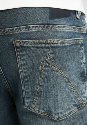 Jeans van denim met een donkerblauwe wassing, zichtbaar stiksel en een kenmerkend zakontwerp. Textuurstof met een lichte vervaging.