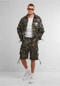 Camouflage-patterned, lightweight fabric jacket and shorts set in dark green and black. Features pockets, drawstrings, and branded patches.