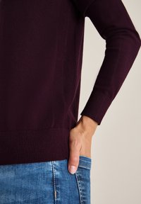 Bordeaux gebreide trui met een aansluitend ontwerp en lange mouwen. Getextureerde stof met geribbelde manchetten en zoom, gecombineerd met blauwe denim.