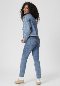Ljusblå denimjacka och byxor i en klassisk design, med fickor och en avslappnad passform. Bärs med beige sneakers och vita strumpor.