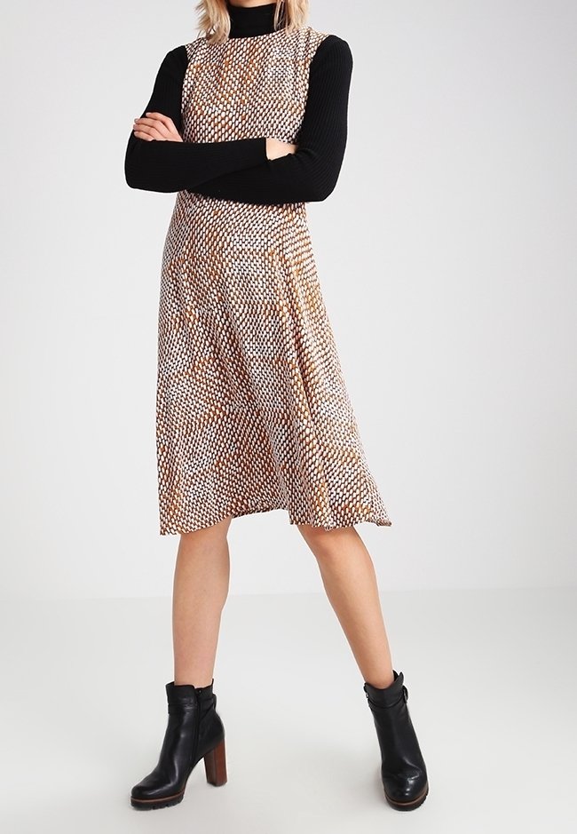 Hame ilman hihoja ruskeasta ja valkoisesta kuviollisesta kankaasta, A-linjan muotoilu, yhdistetty musta pitkähihainen paita ja tukevat mustat korkokengät.