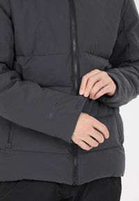 Schwarze Winterjacke mit Reißverschluss, weicher Textur und Klettverschluss an den Ärmelabschlüssen; zeichnet sich durch ein gesticktes Muster aus, das Abschnitte zur Isolierung schafft.