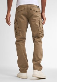 Pantalones cargo beige con bolsillos laterales, un ajuste relajado y detalles de costura visibles. Combinados con zapatillas blancas.