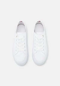 Baskets blanches en toile avec un bout rond, des lacets plats blancs et des œillets argentés. Accents de logo en rouge, blanc et bleu au talon.