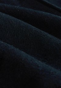 Close-up of dark blue woolen fabric with a soft, fuzzy texture and visible folds creating shadowed ridges.