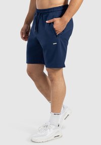 Pantalones cortos azul marino hechos de una tela suave con una cintura elástica, bolsillos frontales y un pequeño logo metálico en el lado izquierdo.