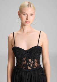 Schwarzes Kleid mit einem durchsichtigen, bestickten Oberteil, das mit Blattmustern verziert ist. Spaghetti-Träger und ein fließender, plissierter Rock.