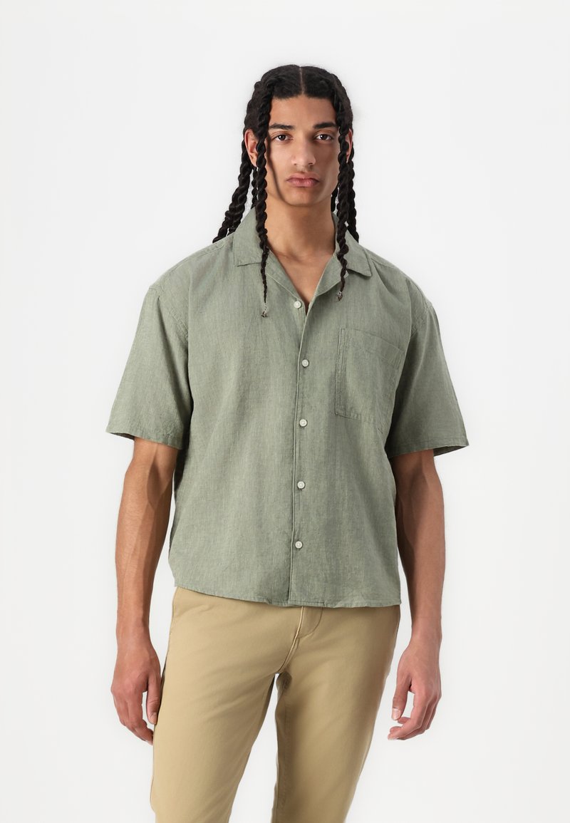 Camicetta a maniche corte, verde oliva, con bottoni e tasca sul petto, realizzata in tessuto testurizzato, con una vestibilità rilassata e un design del colletto.