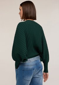 Maglione a coste verde scuro con una vestibilità ampia, caratterizzato da un design testurizzato. Abbinato a jeans in denim azzurro chiaro e una cintura argentata con borchie.