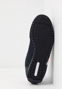 Granatowy but sportowy z teksturowaną czarną gumową podeszwą, siateczkową cholewką i czerwono-białymi-niebieskimi akcentami po bokach.