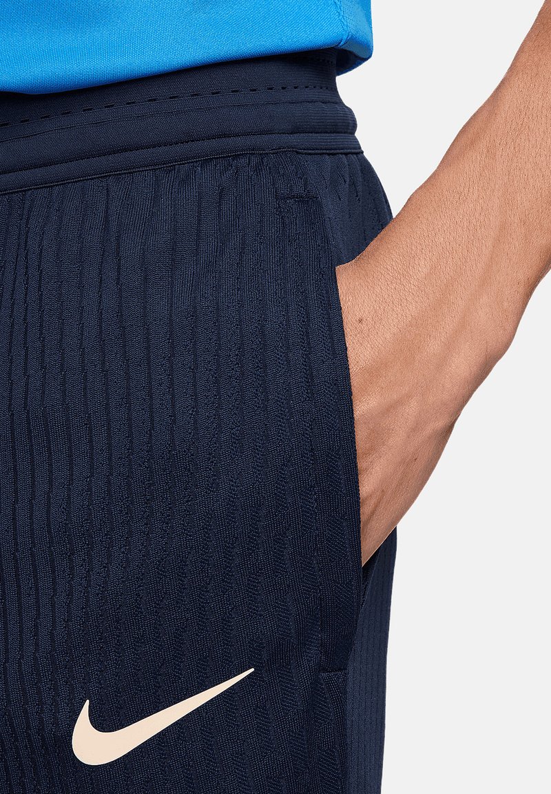 Pantalones cortos deportivos navy con rayas verticales texturizadas, cinturilla elástica y un bolsillo lateral. Presenta un logo de Nike en color crema cerca del dobladillo.