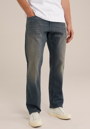 Blue denim jeans with a straight fit, featuring a faded wash, classic five-pocket design, and paired with white sneakers.