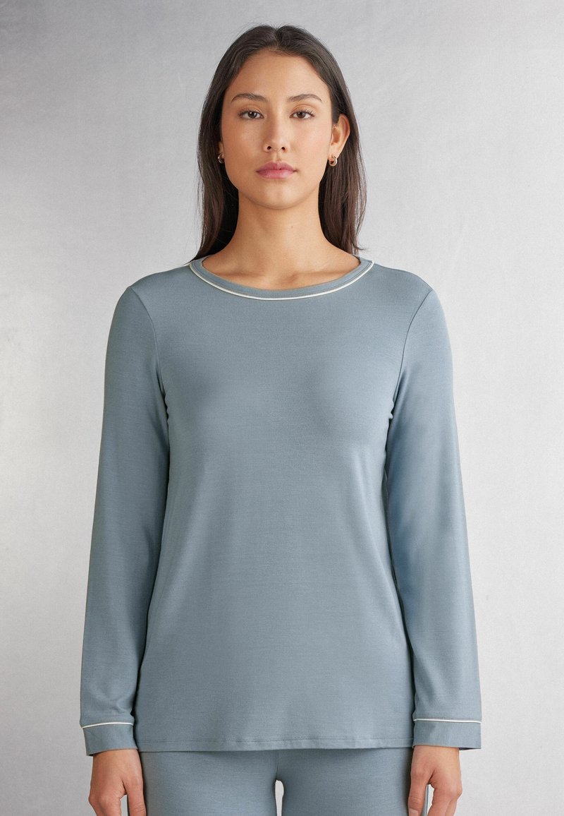 Ljusblå långärmad tröja med rund halsringning och kontrasterande vit sömnad längs kragen och ärmsluten, tillverkad av mjukt material.