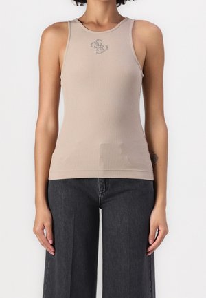 Beige rygstrikket ærmeløs top med lille dekorativt logo ved brystet, båret sammen med høj-taljede mørke bukser med vide ben.