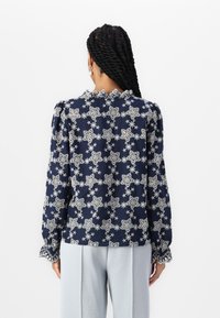 Blusa navale con motivi floreali bianchi, colletto arricciato e maniche a sbuffo. Realizzata in tessuto leggero, presenta cuciture dettagliate sui polsini.