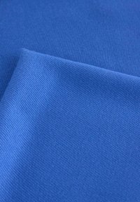 Niebieski kwadratowy kawałek materiału o gładkiej teksturze i drobnym wzorze dziewiarskim, złożony w rogu, odsłaniający jednolity kolor bez wzorów czy akcentów.