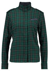 Grüne Karobluse mit hohem Kragen, langen Ärmeln und einer Brusttasche mit Denim-Akzent. Aus einem weichen, strukturierten Stoff gefertigt.