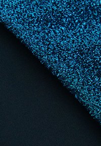 Blått texturerat tyg med en glänsande yta över ett svart ribbat material. Färgerna kontrasterar skarpt och tillför visuellt intresse.