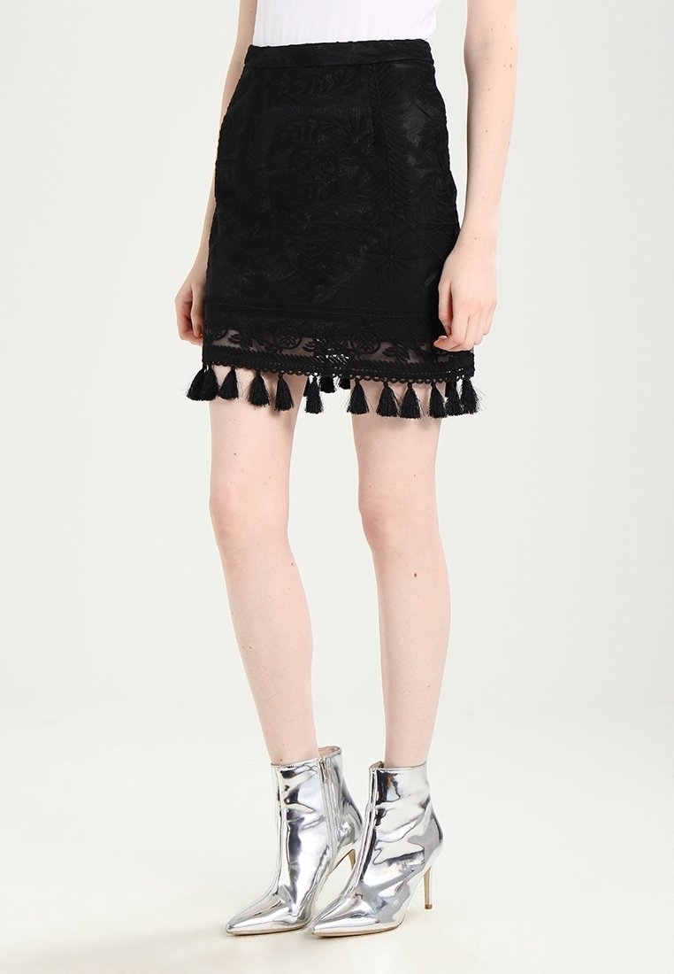 Černá vyšívaná mini sukně s krajkovým lemem a černými třásněmi podél spodního okraje; kombinováno se třpytivými stříbrnými kotníkovými botami.