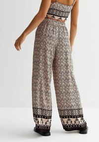 Lekki, wzorzysty spodnie szerokie w kolorze beżowym z czarnymi zygzakami i kwiatowym wykończeniem. Elastyczny pas, w komplecie z dopasowanym topem.
