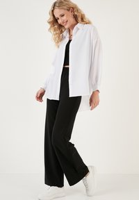Witte blouse met lange, opbollende mouwen, gecombineerd met zwarte, wijde broek en witte sneakers. Glad materiaal en een relaxte pasvorm.