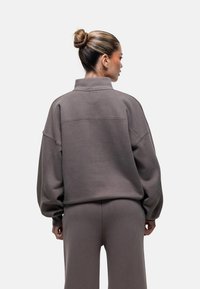 Felpa grigia oversize con colletto alto, spalle scese e polsini a coste, abbinata a pantaloni coordinati, realizzati in un tessuto morbido.