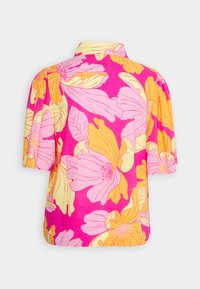 Blouse à manches courtes rose vif avec un grand motif floral jaune et rose clair, et un col simple plié, vue de dos.