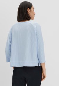 Helles blaues, geripptes Strickoberteil mit dreiviertel Ärmeln, seitlichen Schlitzen und entspannter Passform, von hinten betrachtet.