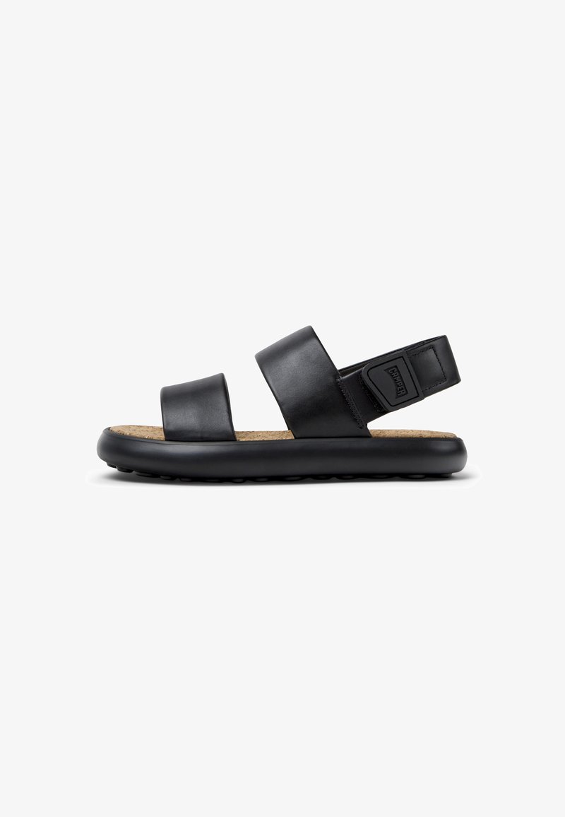 Schwarze Ledersandalen mit zwei breiten Riemen, einem Korkfußbett und einer schwarzen Gummisohle, die kleine, erhabene Punkte für Rutschfestigkeit aufweist.