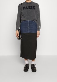 Sudadera gris con estampado "PARIS", combinada con una falda de mezclilla y negra. Zapatos negros y calcetines blancos completan el atuendo. Diseño simple.