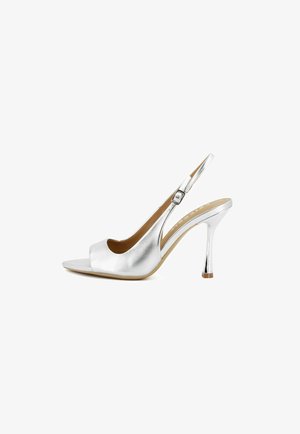 Sandalo slingback argento con tacco alto, punta aperta, fibbia laterale regolabile e tacco sottile e affusolato su sfondo bianco.