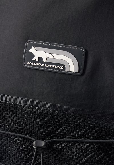 Sac textile noir avec un patch en caoutchouc représentant un renard blanc et un design arc-en-ciel, base en tissu en maille et fermeture à cordon de serrage noir.