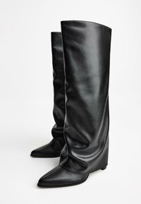 Bottes noires hauteur genou en cuir lisse avec un design loose, bout pointu et petit talon. Présente des coutures discrètes le long des bords.
