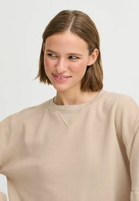 Sweatshirt beige avec un col rond, coupe décontractée et poignets côtelés. Texture lisse, sans motifs ni embellissements. Design simple.