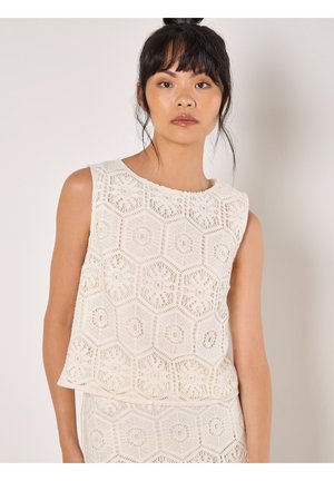Cream sleeveless top with hexagonal crochet pattern and scalloped hem. Soft, textured fabric highlights intricate crochet details.