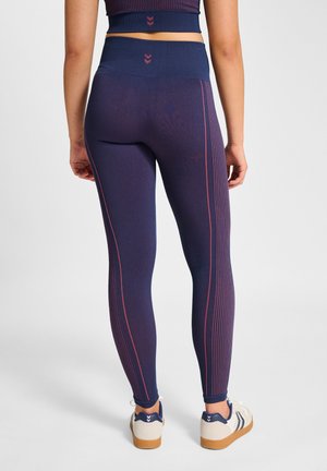 Vrouw draagt marineblauwe leggings met hoge taille en roze verticale strepen, gecombineerd met een bijpassende cropped top en witte sneakers met gumzolen.
