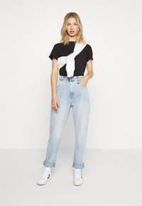 Top preto texturizado de manga curta, sweat branco atado na cintura, jeans de cintura alta de tom azul claro e ténis brancos com detalhes pretos.